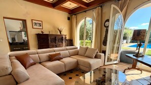 Una sala de estar con un sofá seccional color beige, una mesa de centro de vidrio y vistas a una piscina a través de amplios ventanales.