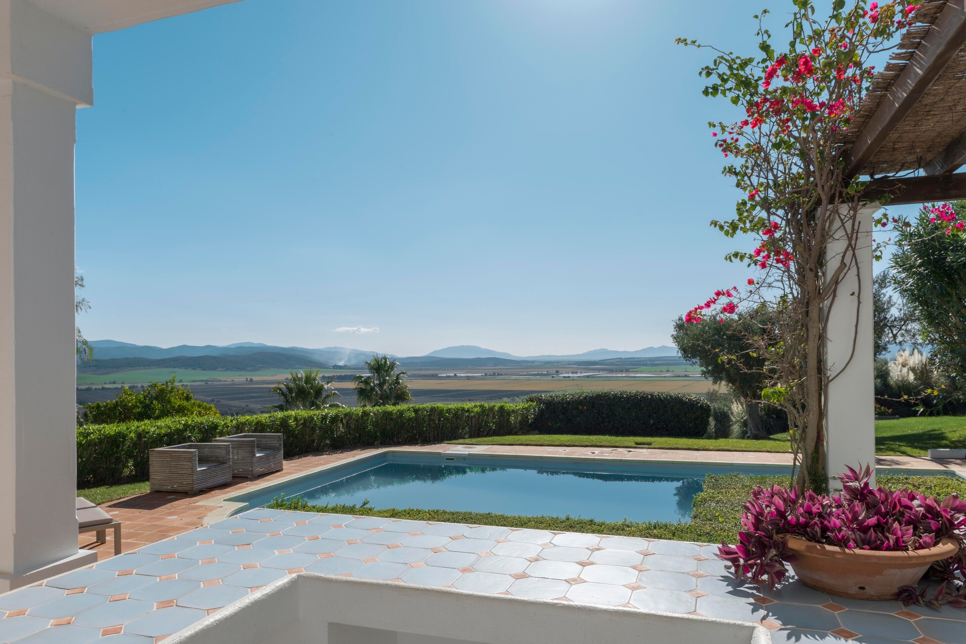 A pool with a clear view of the landscape, a pergola with flowers, and a tiled patio area.