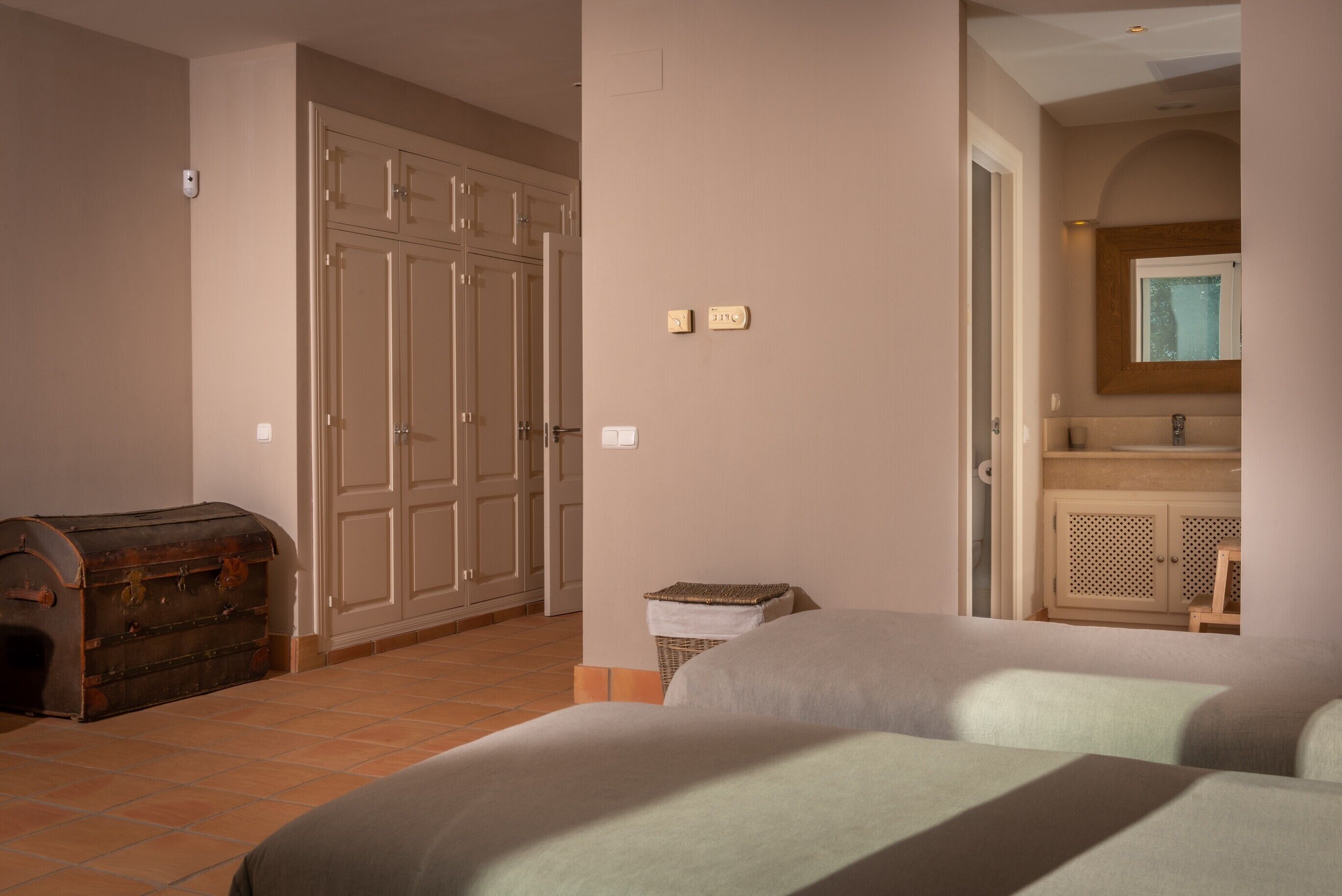 A bedroom with a bed, a wardrobe, a chest of drawers, and a bathroom visible through an open door.