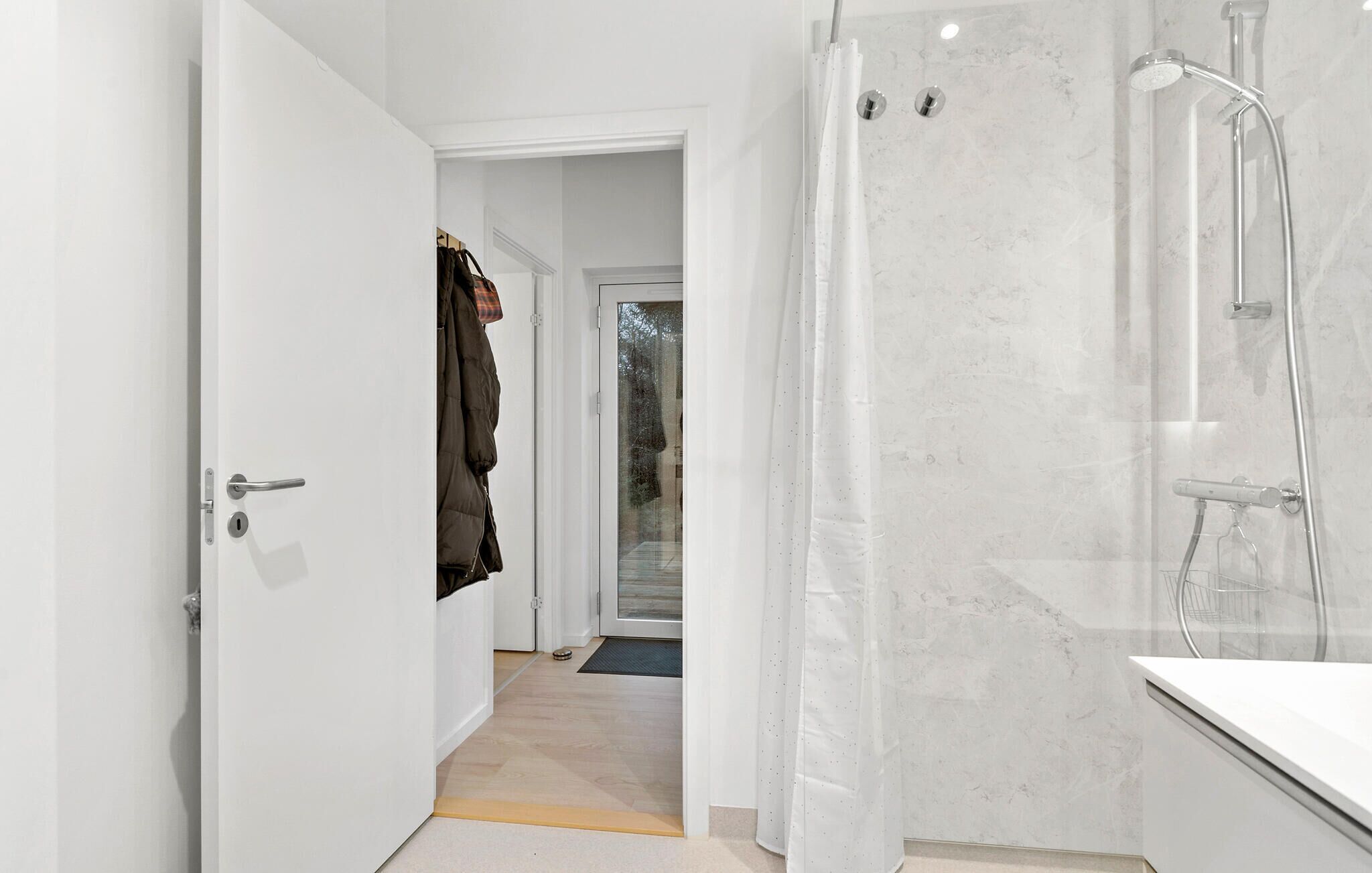 Ein modernes Badezimmer mit Duschkabine aus Glas, einer weißen Badewanne und einer sichtbaren Tür zu einem weiteren Raum.