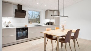 Une cuisine moderne dotée d’un îlot central, d’un four encastré et d’un coin repas avec une table et des chaises en bois.