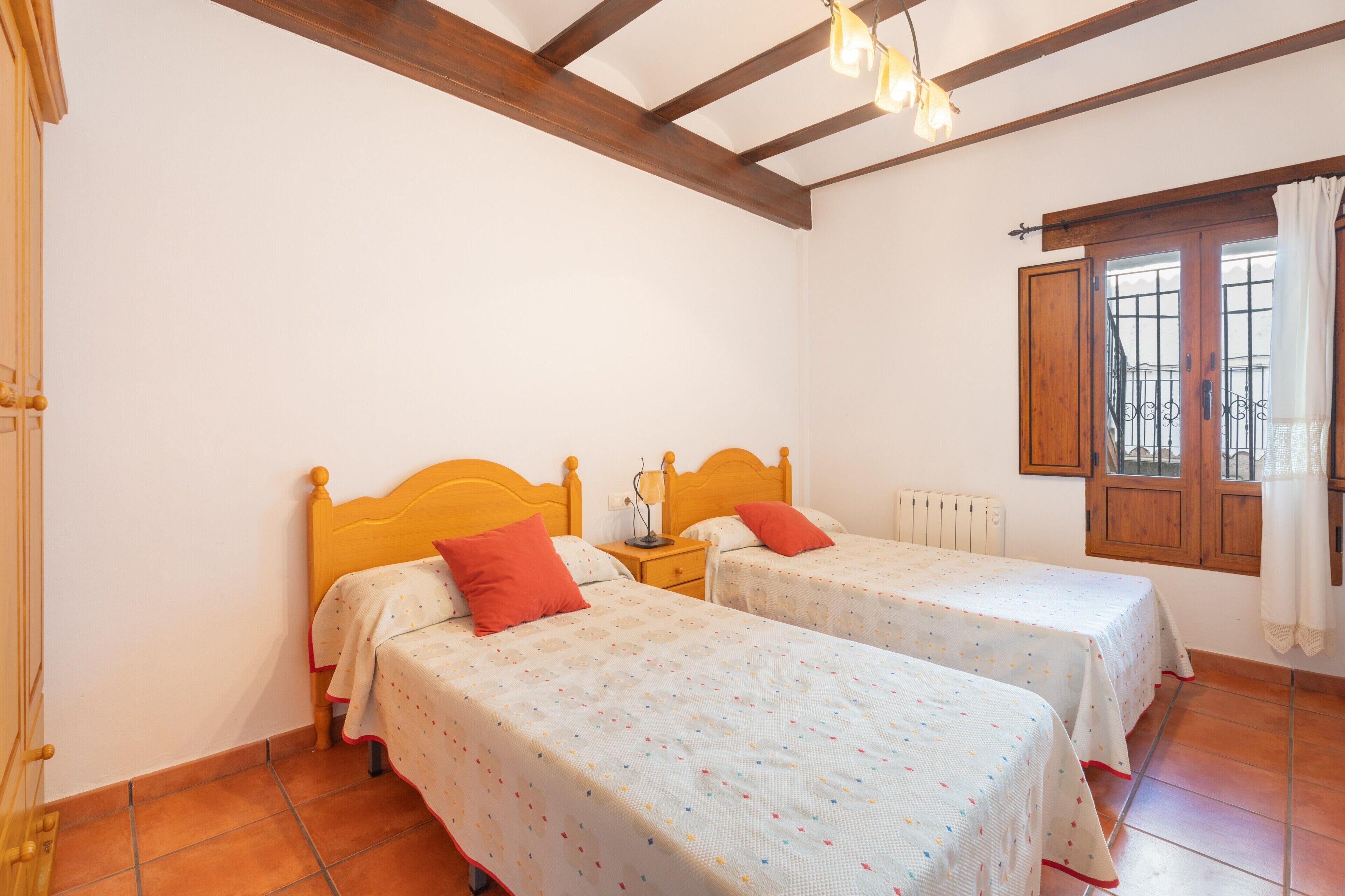 A room with two beds, wooden beams on the ceiling, a radiator, and a window with curtains.