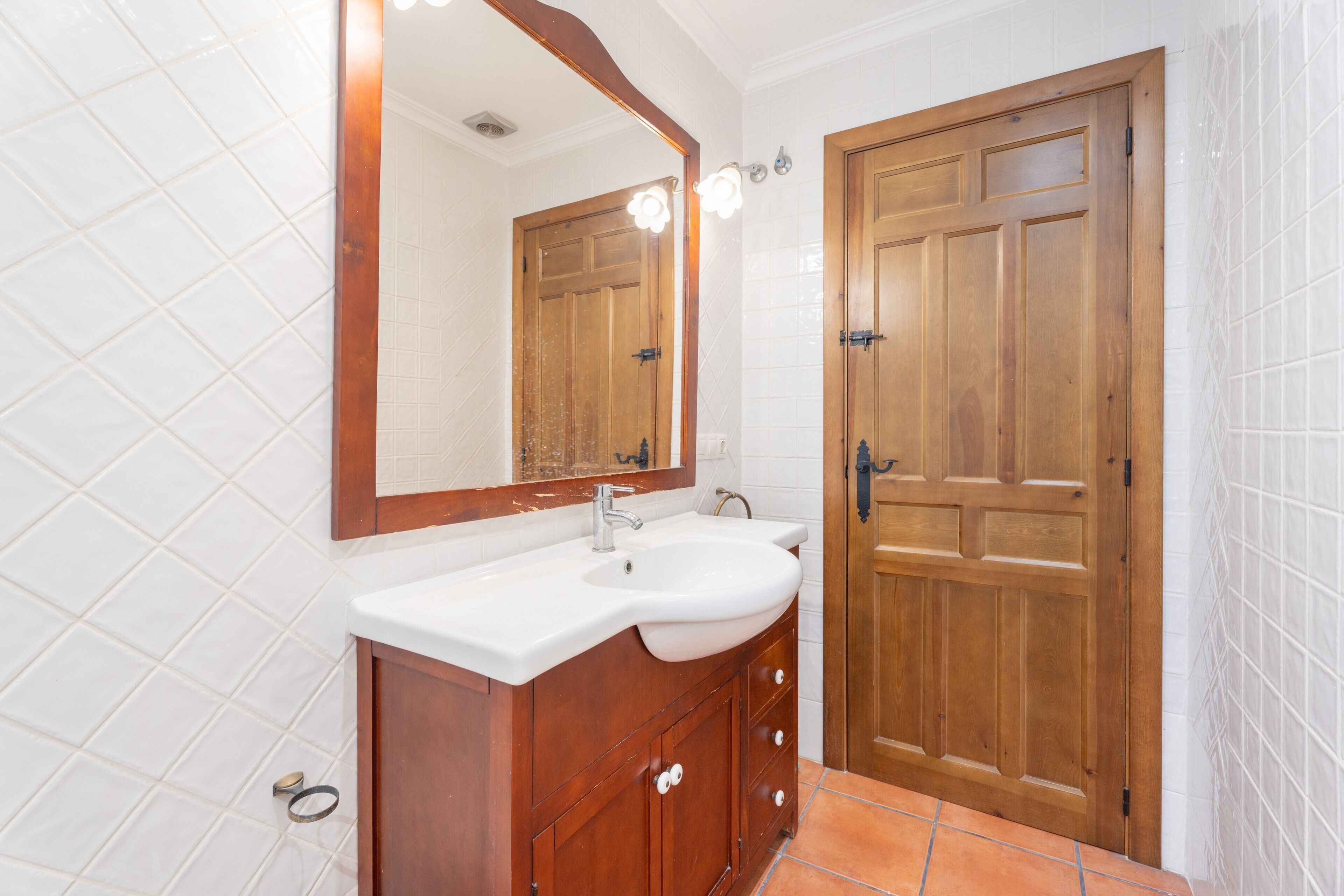 A bathroom with a wooden vanity, a white sink, and a large mirror.