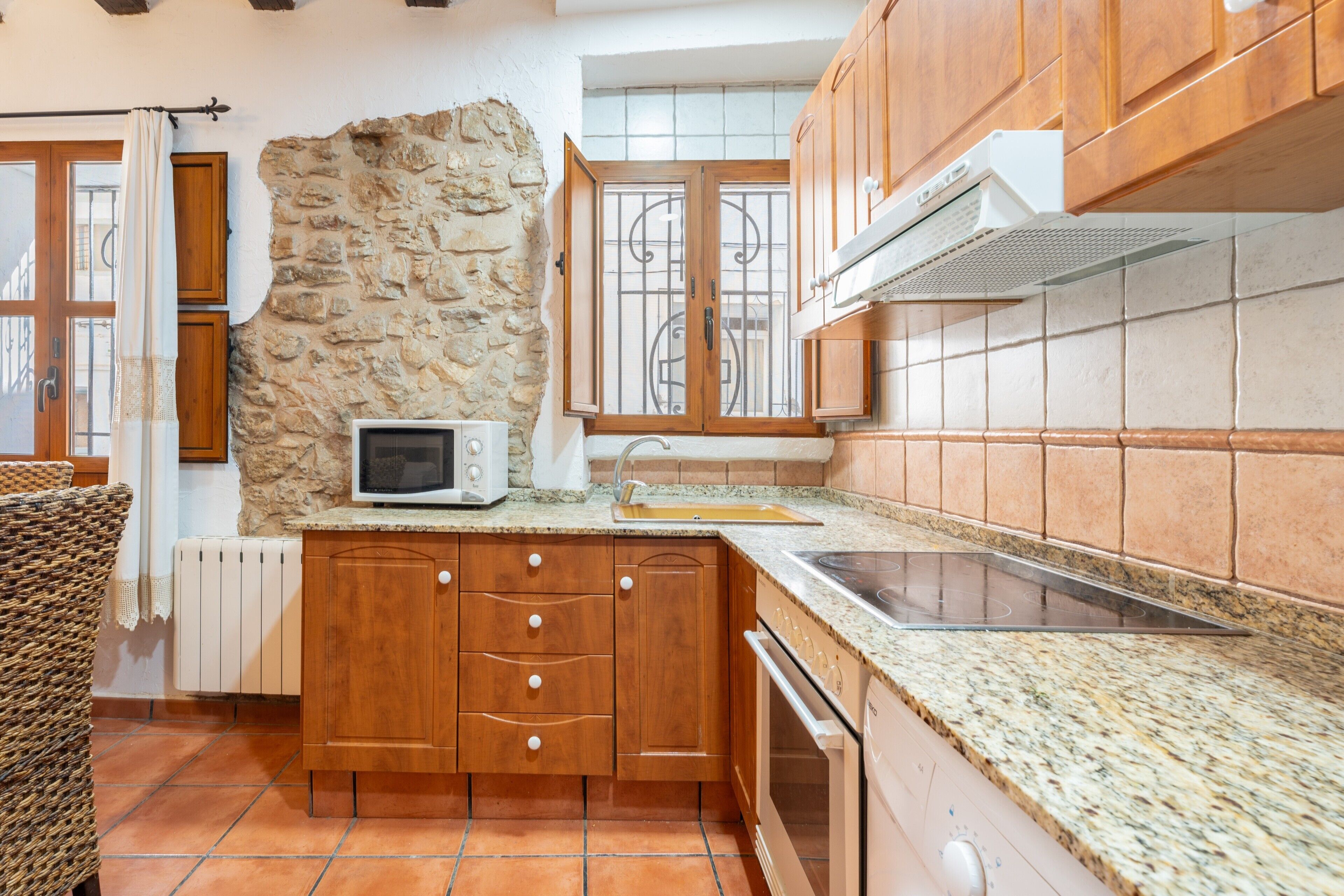 A kitchen with wooden cabinets, a stone wall, a microwave, a sink, and a stove.