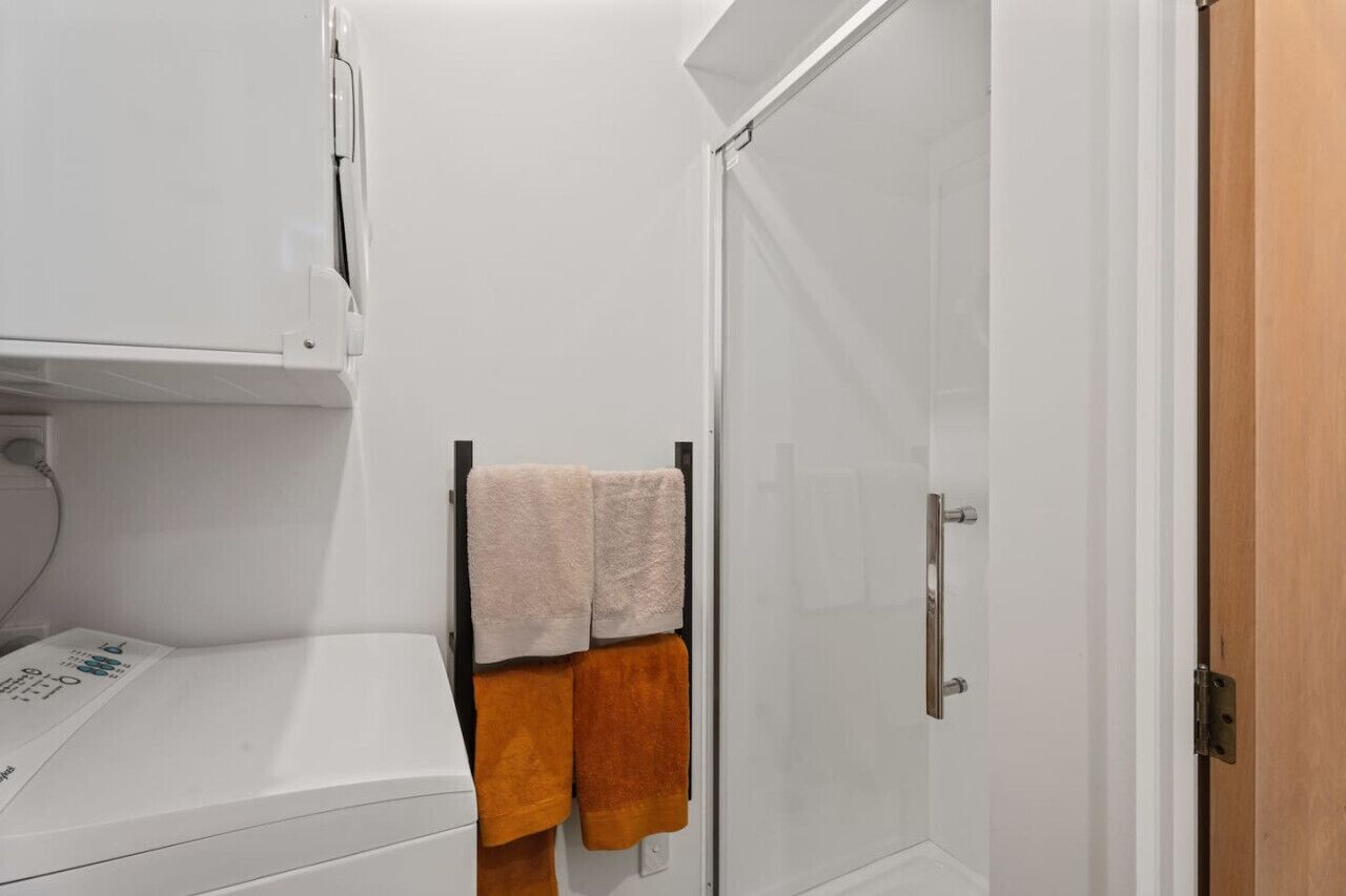 A bathroom with a white sink, a towel rack with a beige towel and an orange towel, and a glass shower door.