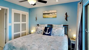 Une chambre à coucher avec un lit, un ventilateur de plafond, un tableau et une table de chevet.