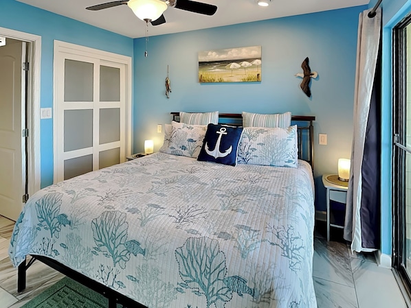 A bedroom with a bed, a ceiling fan, a painting, and a nightstand.
