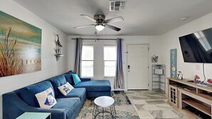 Un salon moderne avec un canapé bleu, un fauteuil rouge, une petite table ronde et un téléviseur posé sur un meuble en bois.