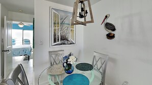 Un coin repas comprenant une table en verre, des chaises, un vase avec des fleurs, un tableau et une décoration représentant un pélican.