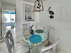 A dining area with a glass table, chairs, a vase with flowers, a painting, and a pelican decoration.