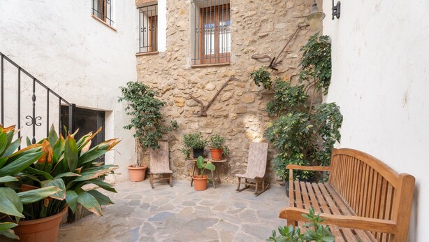 Un patio de piedra con un banco de madera, plantas en macetas y una pequeña mesa.