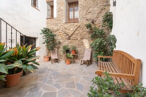 A stone courtyard with a wooden bench, potted plants, and a small table.
