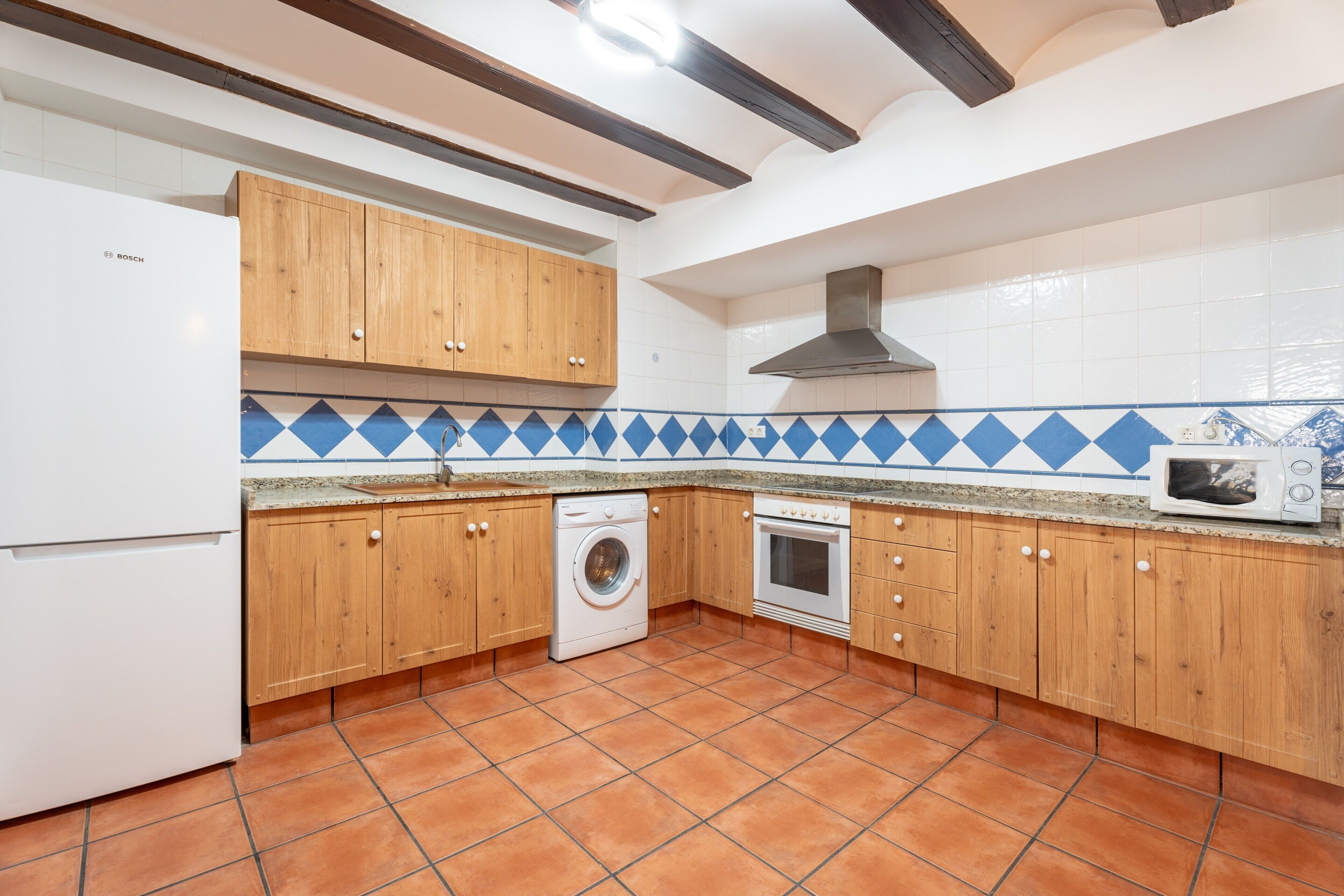 Een keuken met houten kastjes, een wasmachine, een oven en een magnetron.
