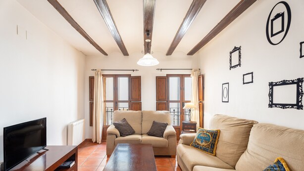 Una sala de estar con sofá, televisión, mesa de centro de madera y techo con vigas a la vista.