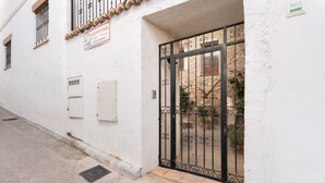 Un edificio blanco con una reja de metal, un cartel y una ventana adosada a un muro de piedra.