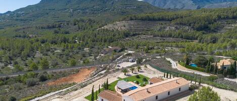 Una propiedad rural con campos escalonados, un edificio blanco con techo de tejas y montañas al fondo.