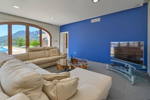 A modern living room with a glass coffee table, beige sofa, and a flat-screen TV. - Villa 'Julie' with Mountain View, Wi-Fi and Air Conditioning (Calpe)