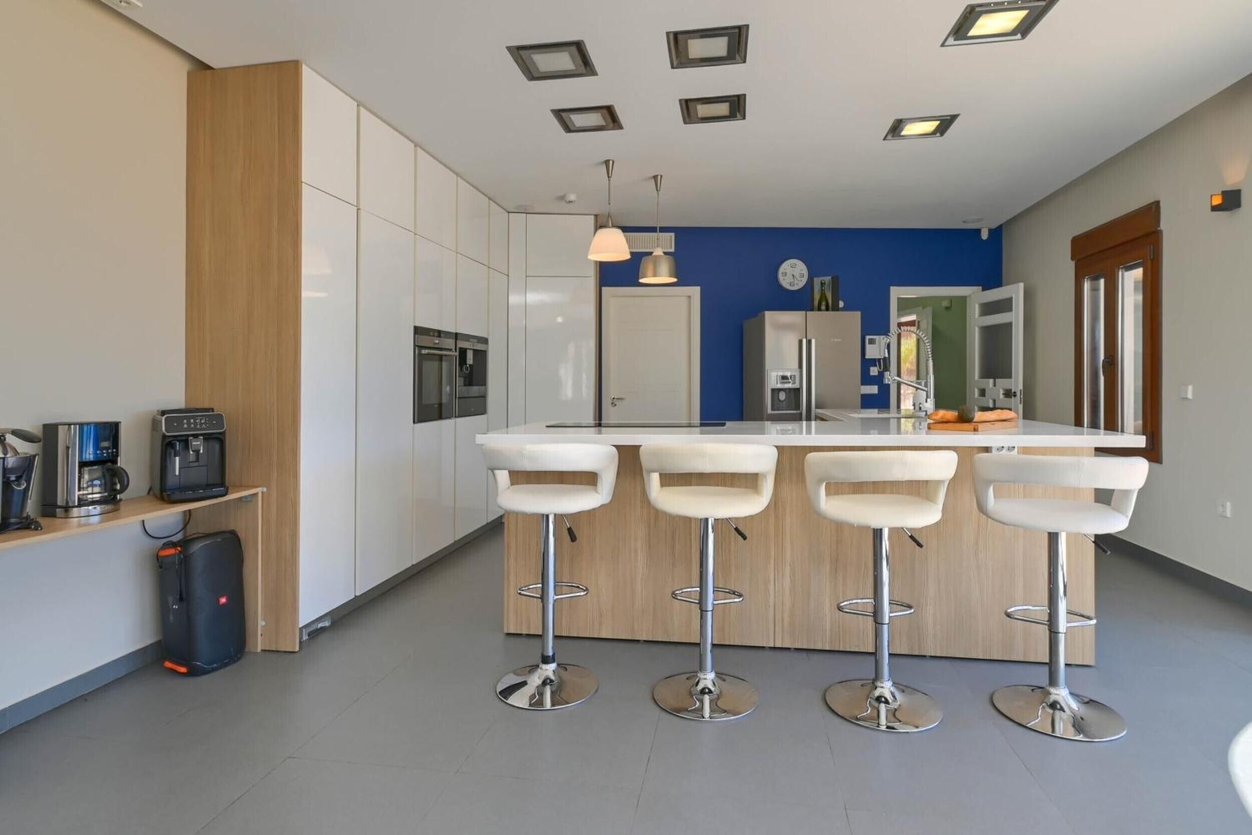 A modern kitchen with white cabinets, a central island with bar stools, and built-in appliances.