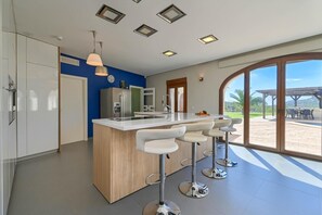 A modern kitchen with a central island, bar stools, and a large window offering a view of the outdoors. - Villa 'Julie' with Mountain View, Wi-Fi and Air Conditioning (Calpe)