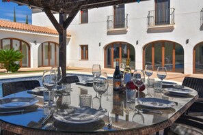 An outdoor dining area with a glass table set for six, surrounded by a white building with arched windows and balconies. - Villa 'Julie' with Mountain View, Wi-Fi and Air Conditioning (Calpe)