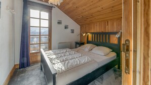 A bedroom with a wooden ceiling, a bed with white bedding, a nightstand with a lamp, and a window with a view of snow-covered mountains. - Apartment 'La Salamandre' with Mountain View, Private Terrace and Wi-Fi (Villard-Reculas)