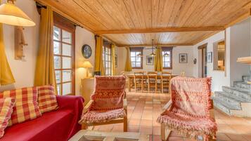 Un salon chaleureux avec un canapé rouge, des fauteuils à motifs, un plafond en bois et un sol carrelé.