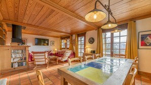 A wooden interior with a tiled floor, a dining table with chairs, a bookshelf, and a sofa. - Apartment 'La Salamandre' with Mountain View, Private Terrace and Wi-Fi (Villard-Reculas)