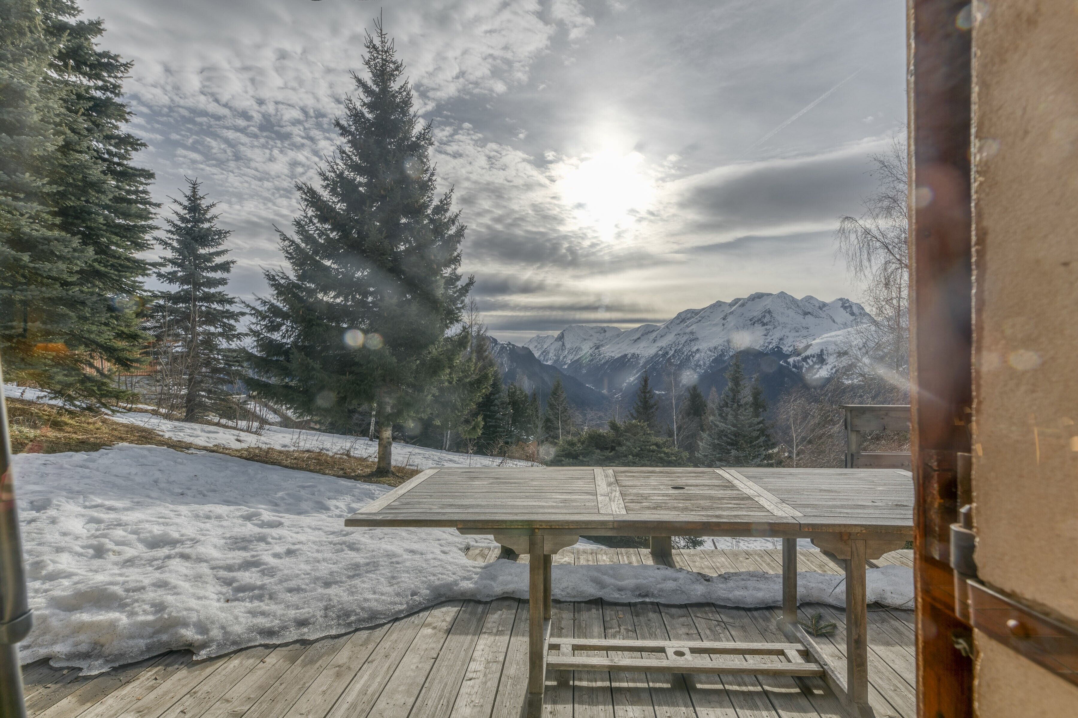 Een houten terras met een tafel, besneeuwde grond en uitzicht op een berg.