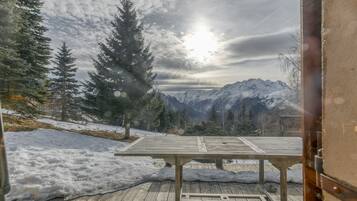 Een houten terras met een tafel, besneeuwde grond en uitzicht op een berg.