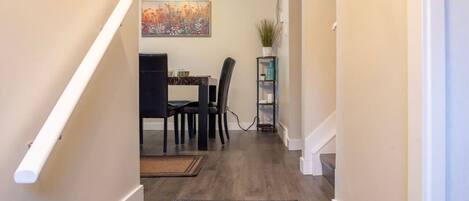 A hallway with a dining area at the end, featuring a dining table, chairs, and a rug.
