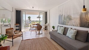 A modern living room with a sofa, chairs, a dining table, and a large window. - Apartment 'Golden Sky' with Shared Pool, Wi-Fi and Air Conditioning (Cabanas de Tavira)