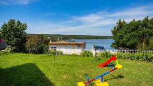 Une zone herbeuse avec une aire de jeux, un bâtiment et une étendue d’eau en arrière-plan.