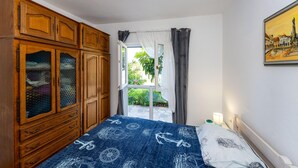 Une chambre avec une grande armoire en bois, un lit avec une literie sur le thème de la marine, une fenêtre avec des rideaux et un tableau accroché au mur.