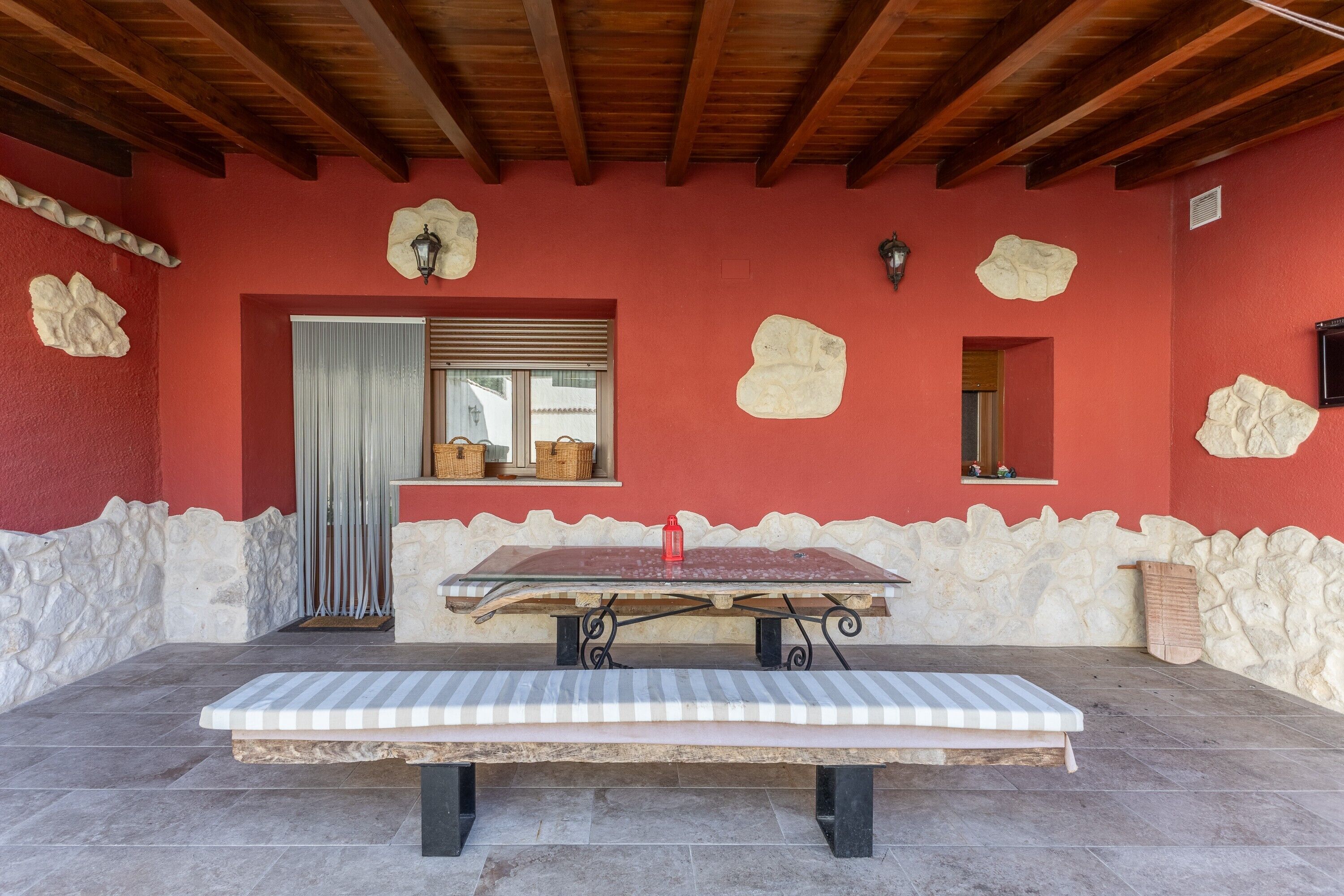 A room with a glass-top table, a bench, stone walls, and a wooden ceiling.