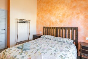 A bedroom with a wooden headboard, a floral bedspread, a hanging clothes rack, and a nightstand.