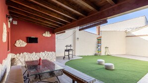 Eine Terrasse mit einem Glastisch, Bänken und einem grünen Kunstrasen.