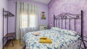 Ein Schlafzimmer mit einem Bett, einem Heizkörper, einem Fenster mit Vorhängen, einem Wäscheständer und einem kleinen Fenster mit Blumen.