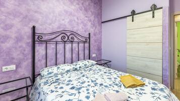 Un dormitorio con una pared morada, un cabecero de cama de metal, una colcha de cama con estampado floral y una puerta corredera de madera.