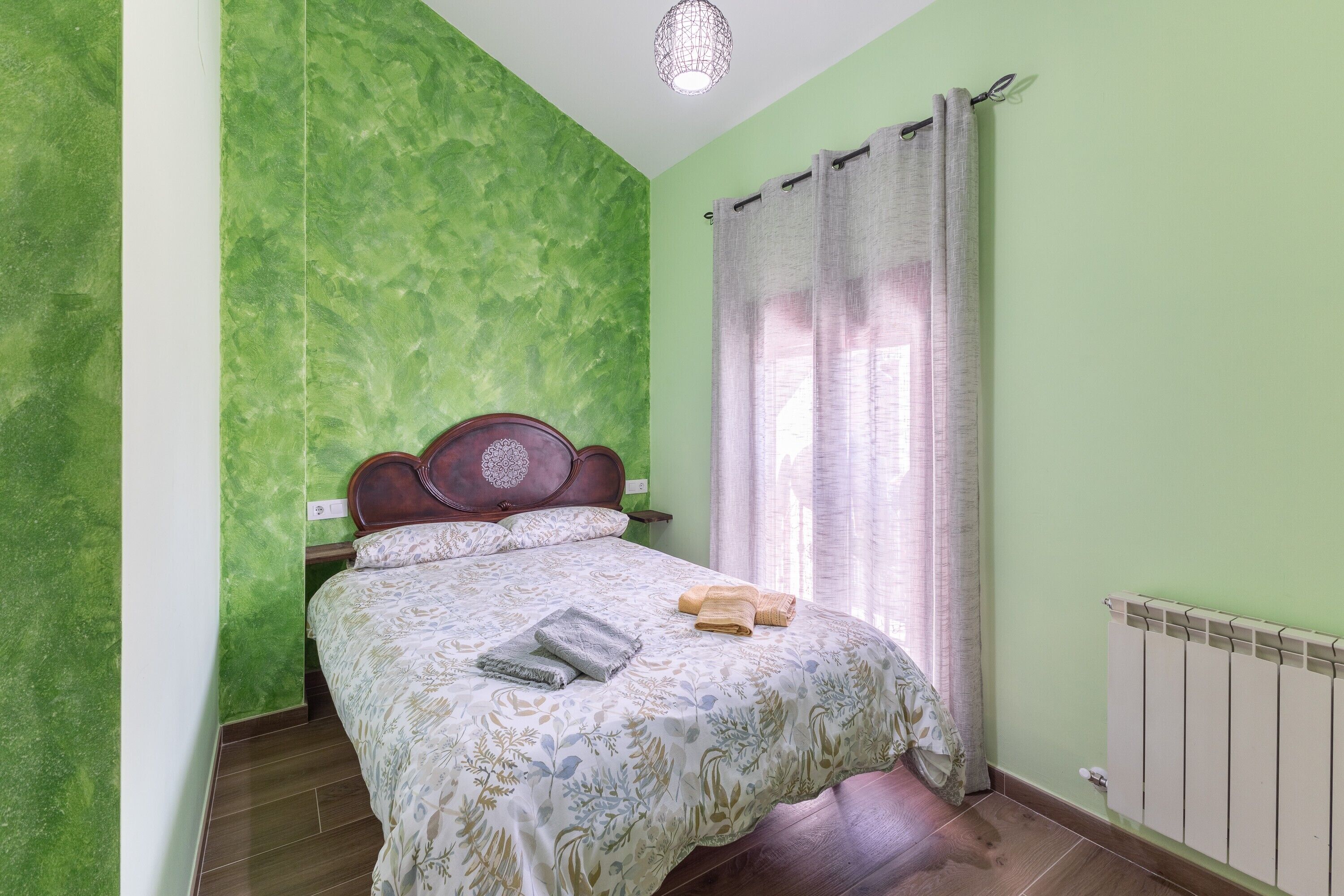 A room with a bed, a wooden headboard, a radiator, and a window with curtains.
