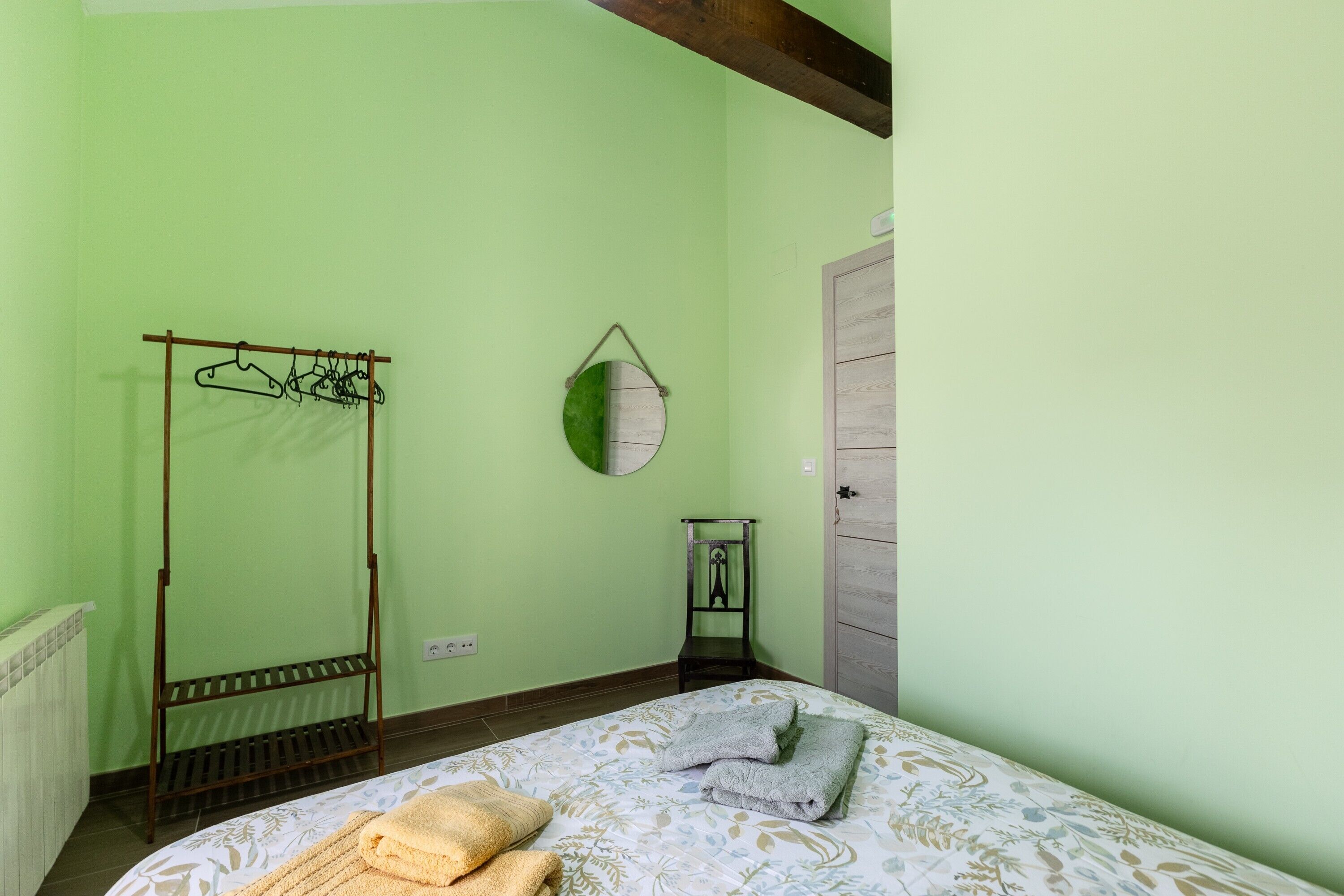 Una habitación con cama, perchero, espejo y puerta.