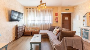 Ein Wohnzimmer mit einer Couch, einem Tisch, einem Fernseher, einer Deckenleuchte, einer Tür und einem Schrank.