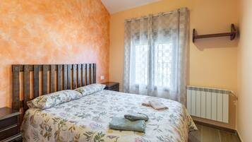 Un dormitorio con cabecera de madera, colcha estampada y radiador, además de una ventana con cortinas.