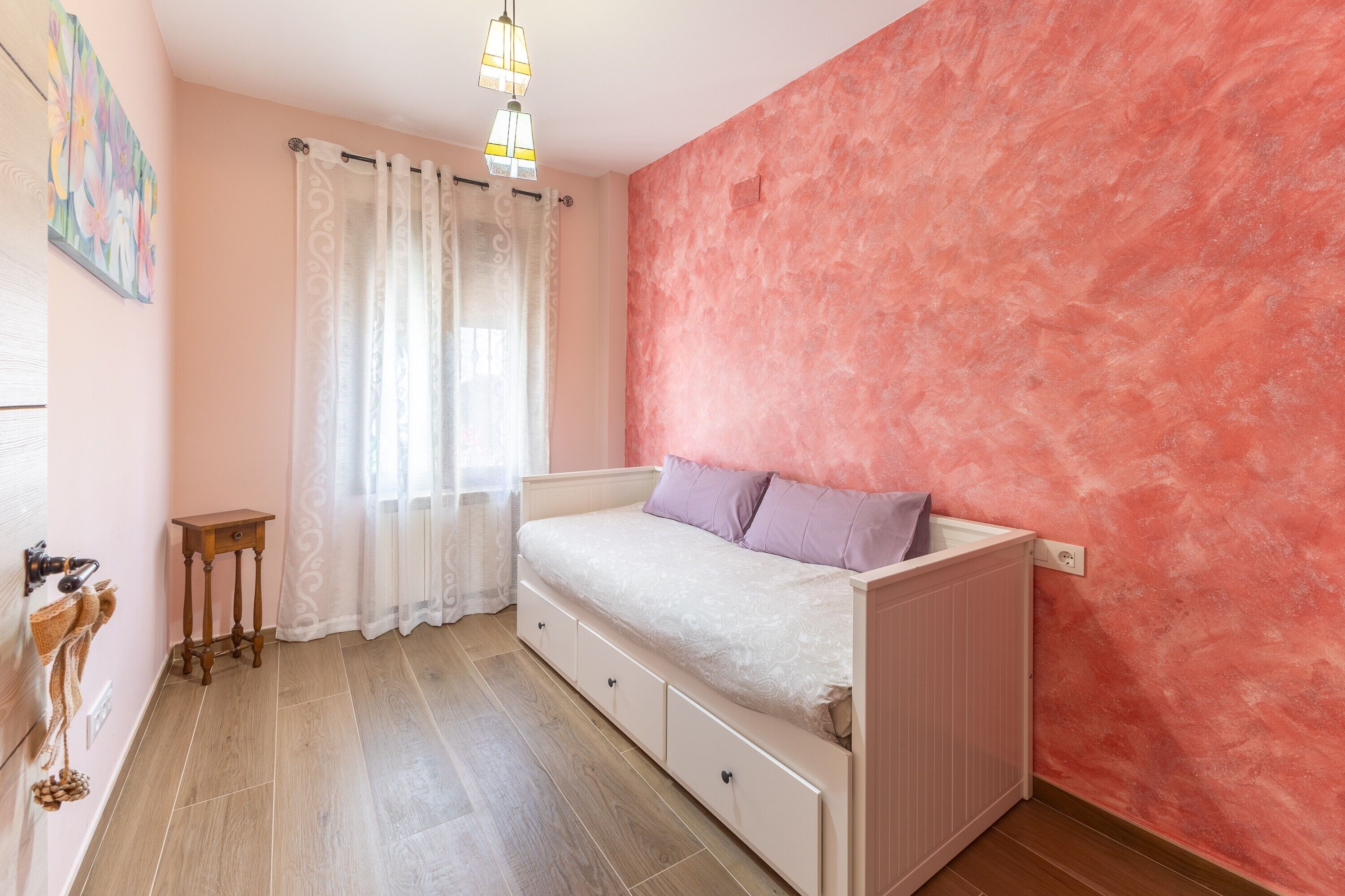 Un dormitorio con cama, una mesita, un radiador y una ventana con cortinas.