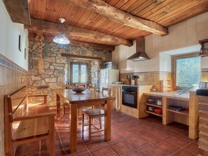 A rustic kitchen with stone walls, wooden beams, a stone fireplace, and a large window.