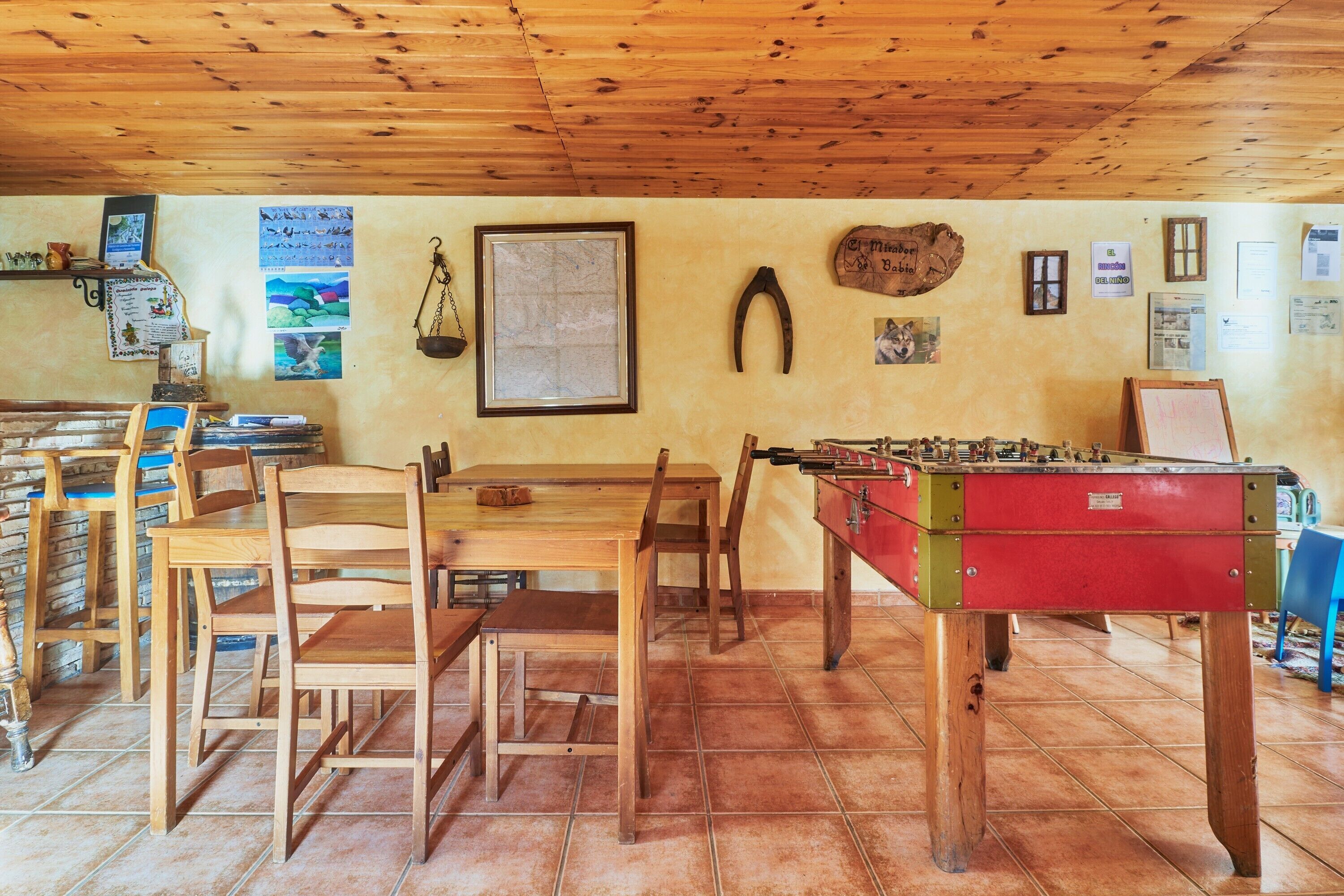 Une pièce au plancher en bois, avec une table de baby-foot, des chaises et une carte accrochée au mur.