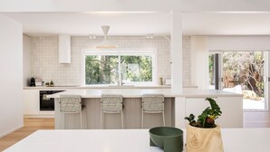 Een moderne keuken met een groot kookeiland, witte kasten en uitzicht op het buitengebeuren.