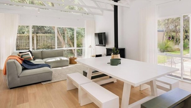 A modern living room with a white table, benches, a grey sofa, and a TV.
