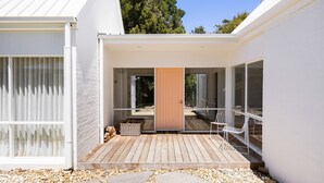 Een modern huis met een houten terras, een schuifdeur en een klein zitgedeelte met stoelen.