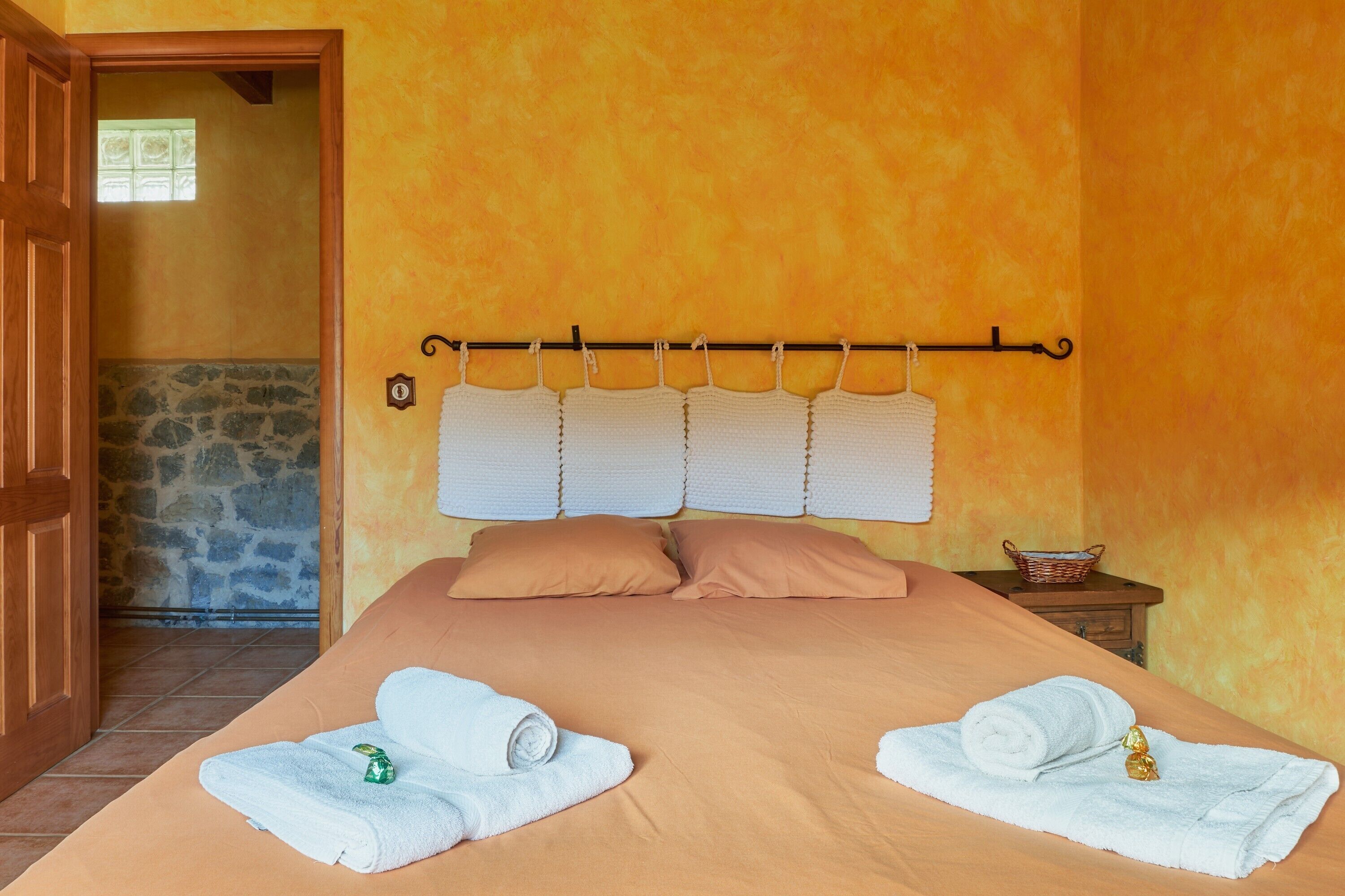 A bedroom with a bed, two towels, a nightstand, and a stone wall.