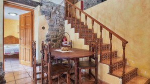 Uma escadaria de madeira com detalhes elaborados, uma mesa redonda de madeira com cadeiras e uma parede de pedra.